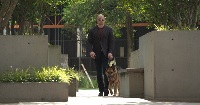 Wide shot of Chad E Foster walking independently past corporate building